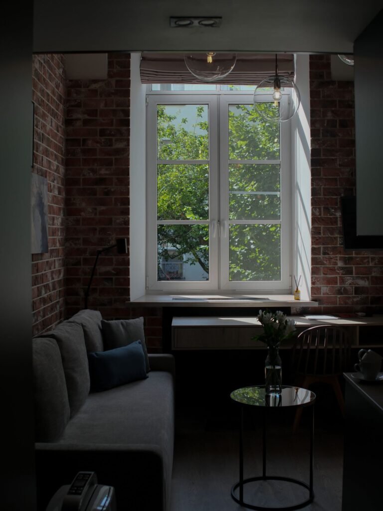 Sunlit brick-walled apartment with a sofa and a working desk beside a large window