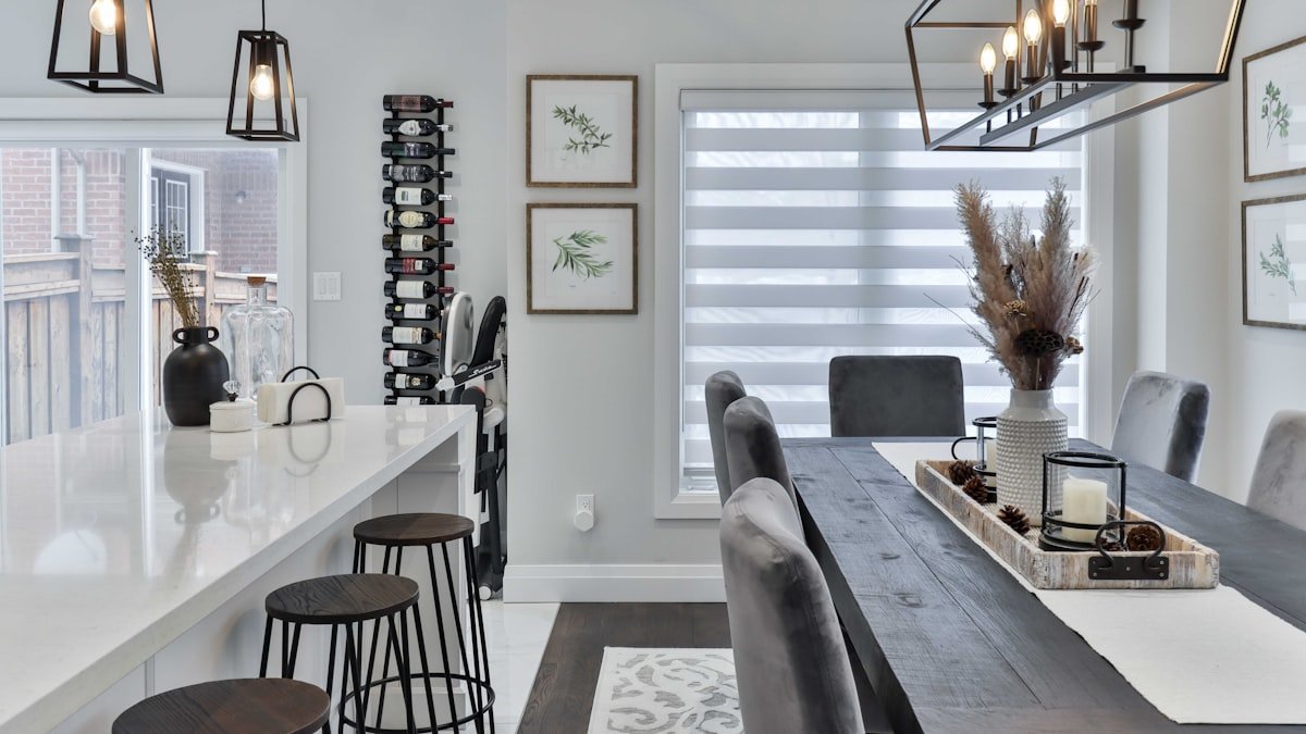 Furnished dining room and kitchen with a long wooden table, grey chairs and a white island with bar stools